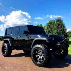 a black jeep parked on the side of a road next to a field and trees