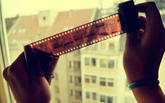 a person holding up a film strip in front of a window with cityscape