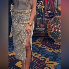 a woman standing in front of a mirror wearing a silver dress and gold bracelets