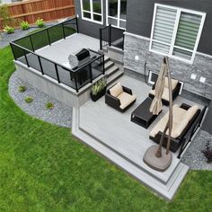 a patio with furniture and an umbrella on the ground in front of a house that is surrounded by grass