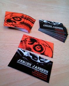 four business cards on a wooden table with orange and black inked designs, each featuring a skeleton