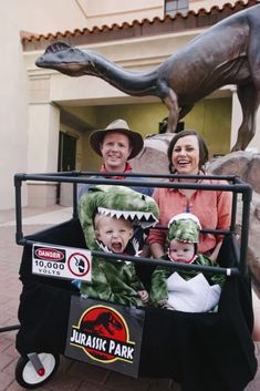 three adults and two children in a cart with a dinosaur statue behind them