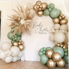 a baby's first birthday party with gold and green balloons, greenery and flowers