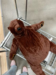 a person standing next to a large brown teddy bear in a shopping cart with wheels