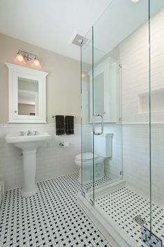 a white bathroom with black and white floor tiles on the walls, shower stall, toilet and sink