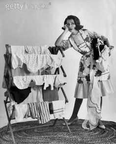 an old photo of a woman standing next to a crib with clothes on it