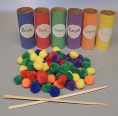 several rolls of colored pom poms next to two wooden sticks and some cotton balls