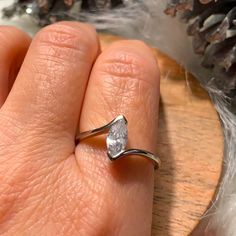 a person's hand holding a ring with a white diamond on the middle of it