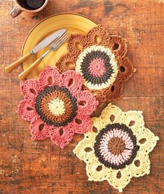 three crocheted doily sitting on top of a wooden table next to a cup of coffee