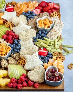 a wooden platter filled with fruit, crackers and pretzels