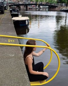 a woman sitting on the edge of a body of water next to a yellow hose