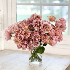 a vase filled with pink flowers sitting on top of a table next to a window