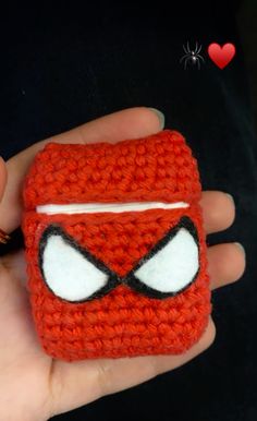 a hand holding a small crocheted toy with eyes on it's face