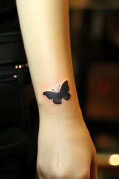 a small black butterfly tattoo on the left wrist and right hand is shown in front of a woman's arm