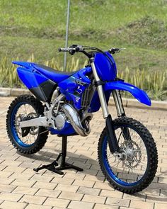 a blue dirt bike parked on top of a brick road