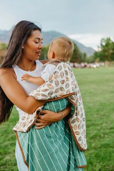 a woman holding a baby in her arms while standing on top of a grass covered field