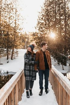 a man and woman walking across a bridge in the snow