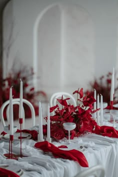 the table is set with white and red flowers, candles, and napkins on it