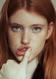 a woman with freckles on her face and finger to her lips, posing for the camera