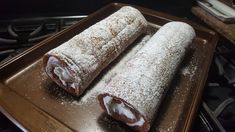 two pastries sitting on top of a baking pan covered in powdered sugar and icing