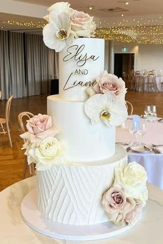 a three tiered wedding cake with flowers on the top is displayed in a banquet room