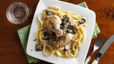 a white plate topped with pasta covered in chicken and mushrooms next to a fork and knife