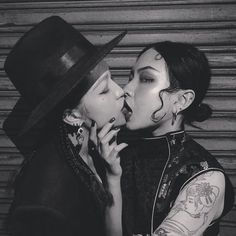 two women are kissing each other while wearing black hats and piercings on their ears