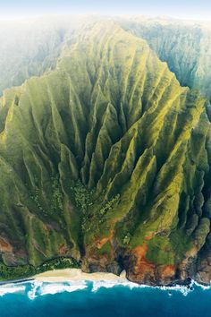 an aerial view of the green mountains and ocean with waves crashing on them, taken from above