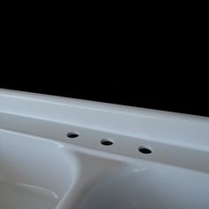 a white sink with four holes in the front and two on the back, against a black background