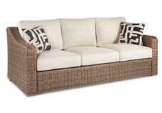 a wicker couch with two pillows on the back and one pillow on the side