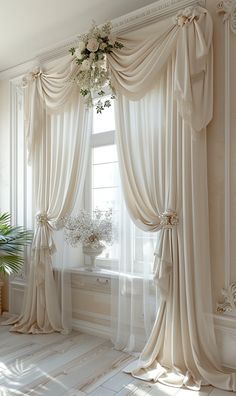 a white room with curtains and flowers on the window sill