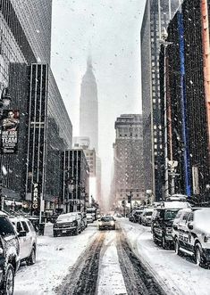 cars driving down a snow covered street with tall buildings and skyscrapers in the background