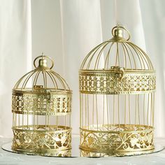 two golden birdcages sitting next to each other on top of a white table