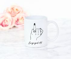 a white coffee mug with the word engaged af written on it and a pink rose in the background