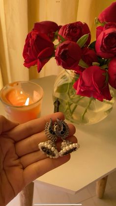 a person holding two rings in their hand next to a vase with red roses on it