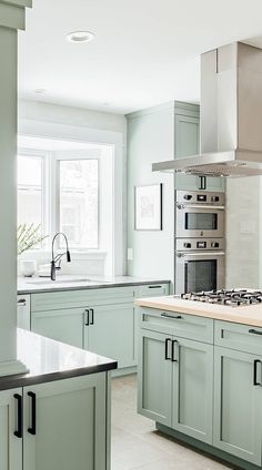 a kitchen with light green cabinets and white counter tops is pictured in this image, there are two windows above the stove