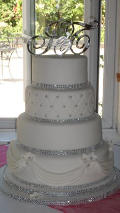 a three tiered wedding cake with diamonds on the top and bottom, sitting in front of a window