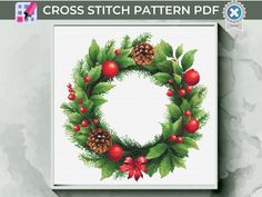 a cross stitch christmas wreath with pine cones and holly berries on the front is shown