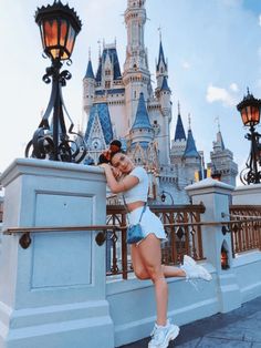 a woman leaning on a railing in front of a castle at disney world with her hands behind her head