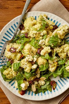 a white plate topped with spinach and cauliflower next to a fork on top of a wooden table