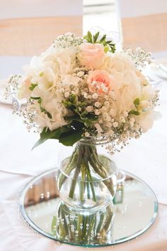 a vase filled with white and pink flowers on top of a glass table covered in silverware