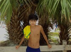 a shirtless young man standing next to a palm tree and holding a yellow frisbee