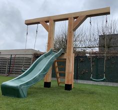 a wooden swing set with a slide in the middle of it and some green grass