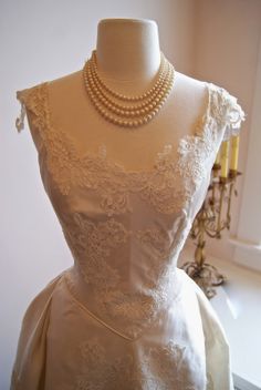 a white wedding dress on display in a room with candles and other items behind the mannequin