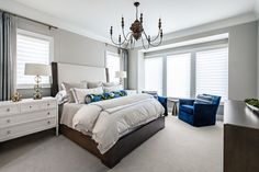 a bedroom with a large bed and blue chairs in front of the window, along with a chandelier