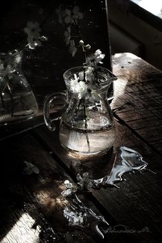 a glass pitcher filled with flowers on top of a wooden table