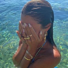 a woman standing in the water covering her face with both hands and looking at the camera