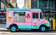 a pink and blue ice cream truck parked on the side of the road next to a white car