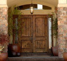 the entrance to a home with two large wooden doors and potted plants on either side