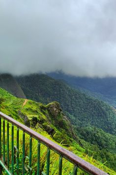 a balcony overlooking a lush green valley with mountains in the distance and clouds hovering overhead